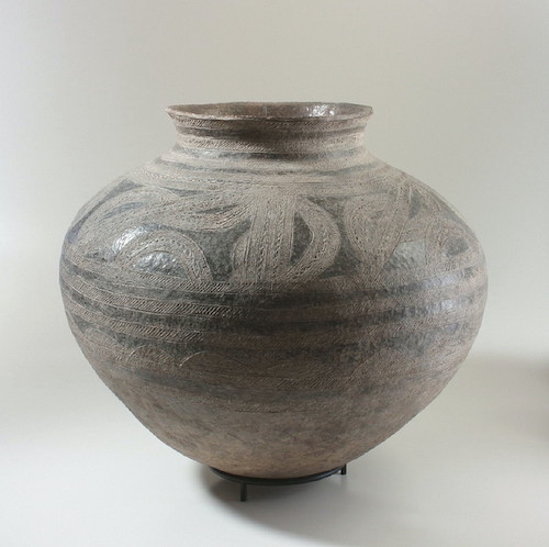 A stout vessel with a pointed bottom, wide shoulders, and a short, slightly flaring neck. The exterior is decorated with horizontal incised bands, and some bands with abstract patterns.