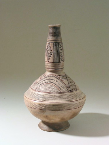 A clay vessel with a small, flaring base; a roughly spherical body with a crest around the waist; and a tall, narrow neck, swelling slightly in the center, then tapering to a narrow rim. The neck and the shoulder of the vessel's body are decorated with complex linear and geometric patterns, using dark red and black pigment on a cream base.