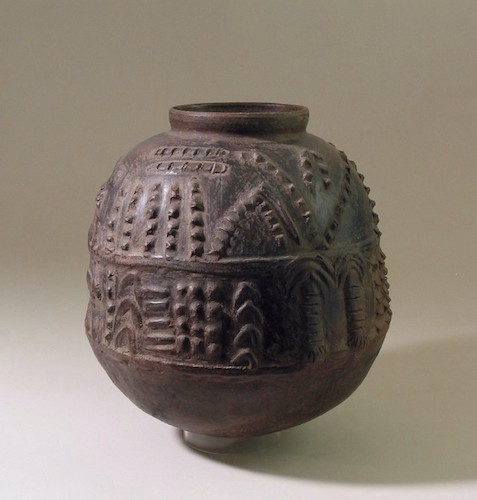 The exterior of the vessel is decorated with two raised bands that encircle the jar at its waist level. The surface of the jar is covered with raised clay pictographic motifs (animal, human, and plant forms) within and above the horizontal bands.
