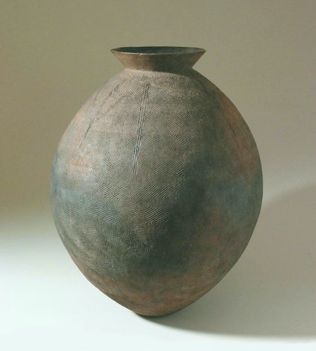 A tall, rounded form with a small flared neck. There is a pressed pattern over the exterior with shallow incised vertical designs around the surface of the shoulder.