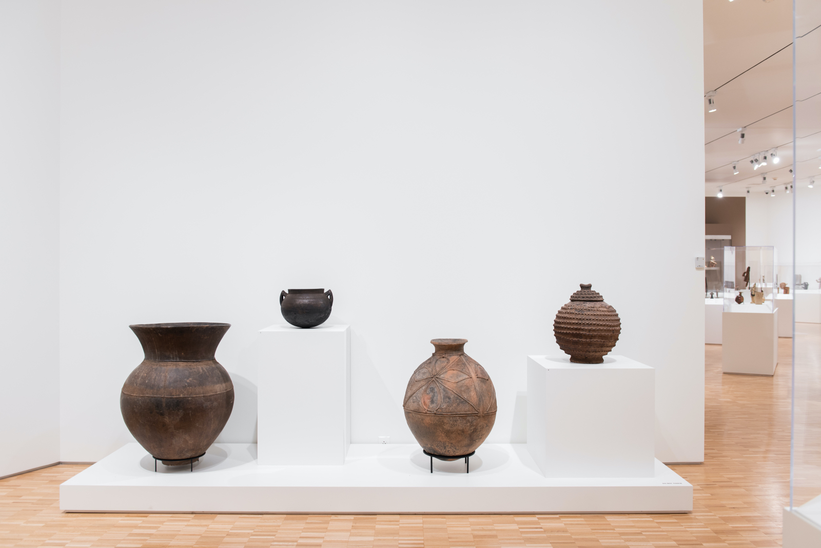 Four brown ceramic pots in different sizes are shown on white pedestals. They all feature different techniques and textures to the ceramic.