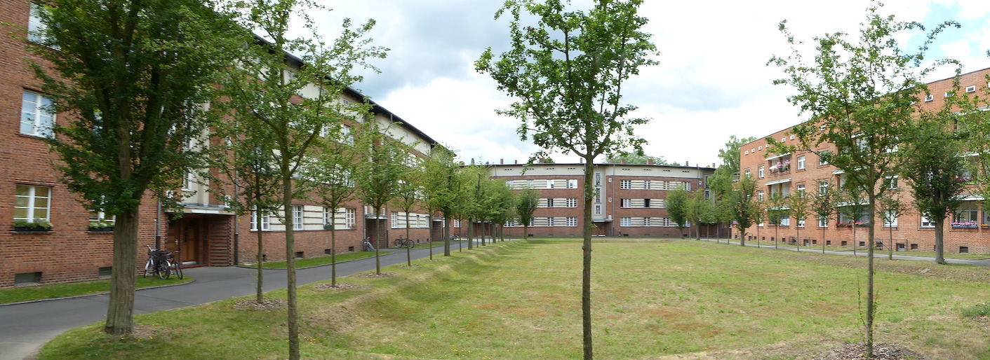 Long three- and four-story brick buildings are arranged around a central grassy courtyard. Trees are planted around the perimeter of the courtyard.