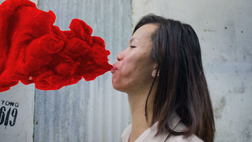 A person is shown in side profile with pursed lips, exhaling a cloud of vibrant red smoke.