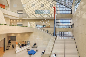 A photograph of a sun-filled building atrium with buff-colored concrete walls and a glass skylight ceiling.