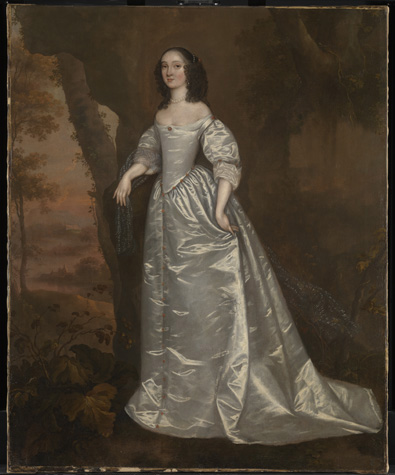 A woman with light skin, dark shoulder-length curls, and a shiny silver gown stands in front of a dark landscape background with trees.