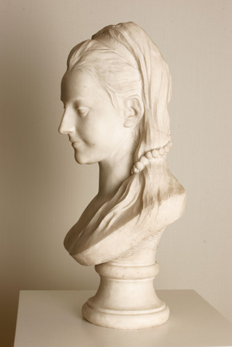 An all-white portrait bust of the head of a young woman who gazes downard. She wears a scarf over her hair, holding it back away from her face.