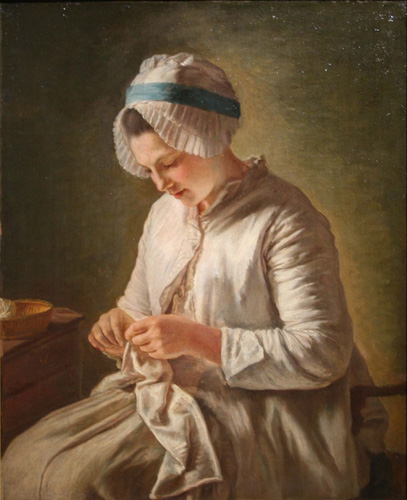 A light skinned young woman wearing a long-sleeved white jacket and white bonnet with blue band is doing needlework in her lap.