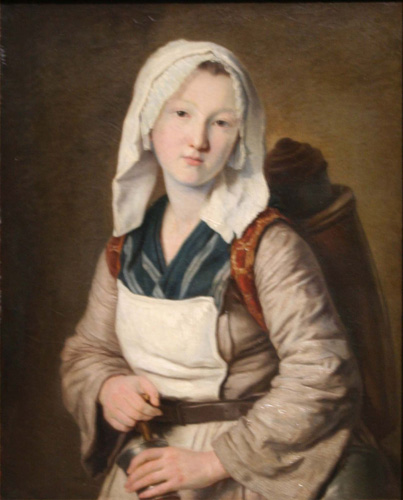 A light-skinned young woman with a long cloth cap and brown adn blue dress is looking out at the viewer. She is wearing some kind of rucksack or pack on her back with items inside it barely visible in the background.