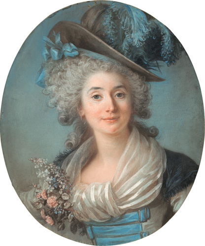 A woman with light skin and curly gray hair is shown from the chest up. She wears an outfit that includes a large dark gray hat with blue ribbons, bows, and feathers, along with a striped white shawl tied around her neck and decorated with a corsage of small flowers.